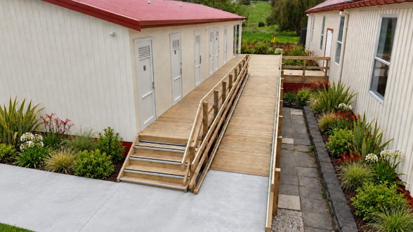 Accessible timber ramp and steps leading to the ablution block at Otamatea Marae, with landscaped gardens